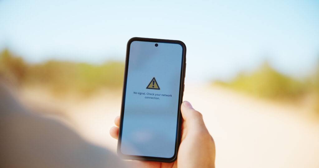 A hand holds a phone with the words “No signal. Check your network connection.” on the screen, indicating that there is no signal.